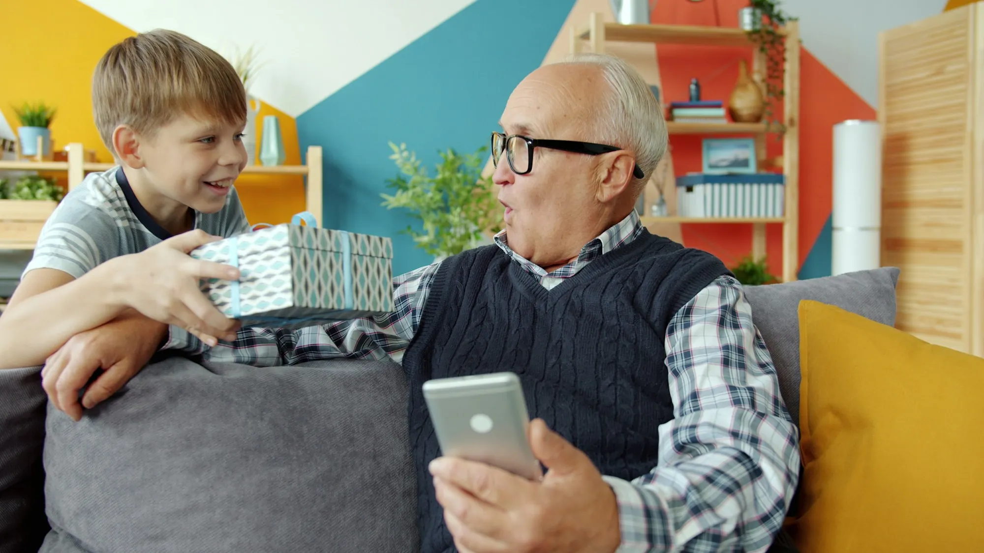 Grandfather opening a gift from his grandson on the sofa